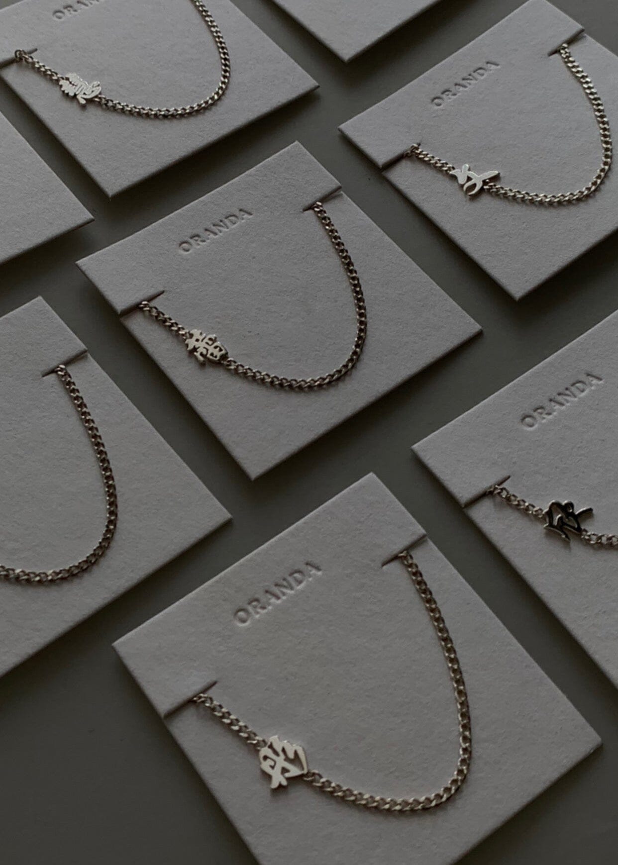 Collection of silver chinese name necklaces on display cards with 'Oranda' branding.